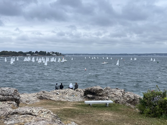 A group of people sitting on a rock overlooking sailboatsDescription automatically generated