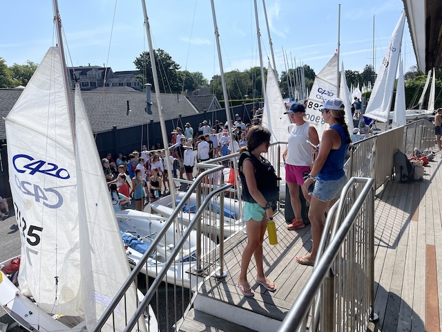 A group of people on a dock with sailboatsDescription automatically generated